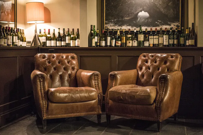 Two brown leather armchairs in front of a bar lined with wine bottles and a large framed picture