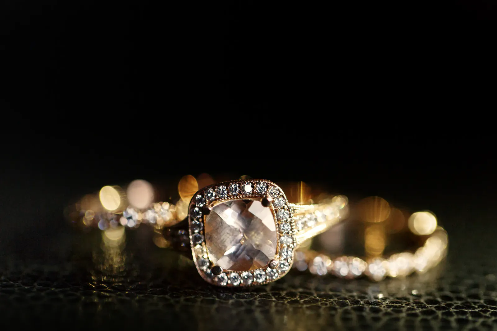Close-up of a rose gold engagement ring with a cushion-cut morganite center stone and diamond halo on a dark textured surface