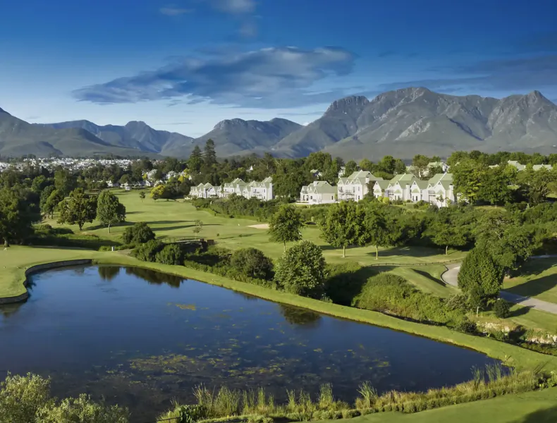 Luxury golf estate with pond, fairways, and mountain backdrop under blue sky