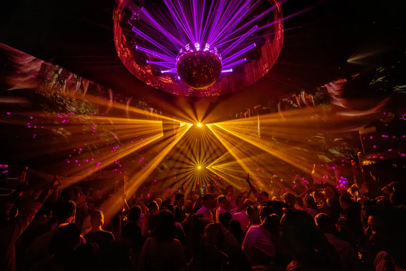 Crowd dancing under purple disco ball and golden light beams at Chinois Ibiza nightclub
