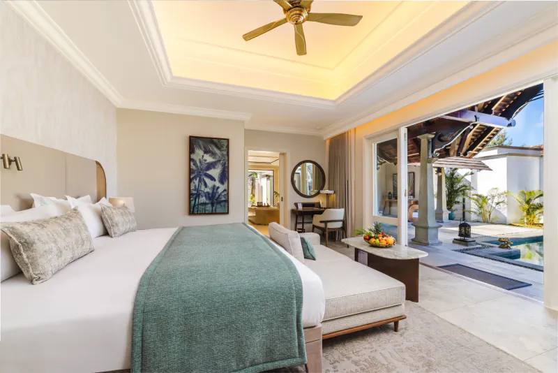 Luxury hotel bedroom with large white bed, green throw, open doors to private pool and ocean view