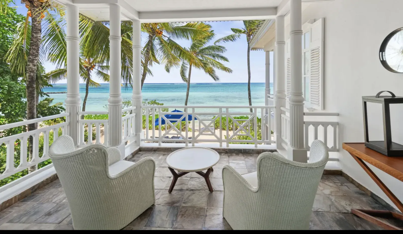 Oceanfront veranda with two white wicker chairs, round table, and palm trees overlooking turquoise sea at Heritage Le Telfair Mauritius