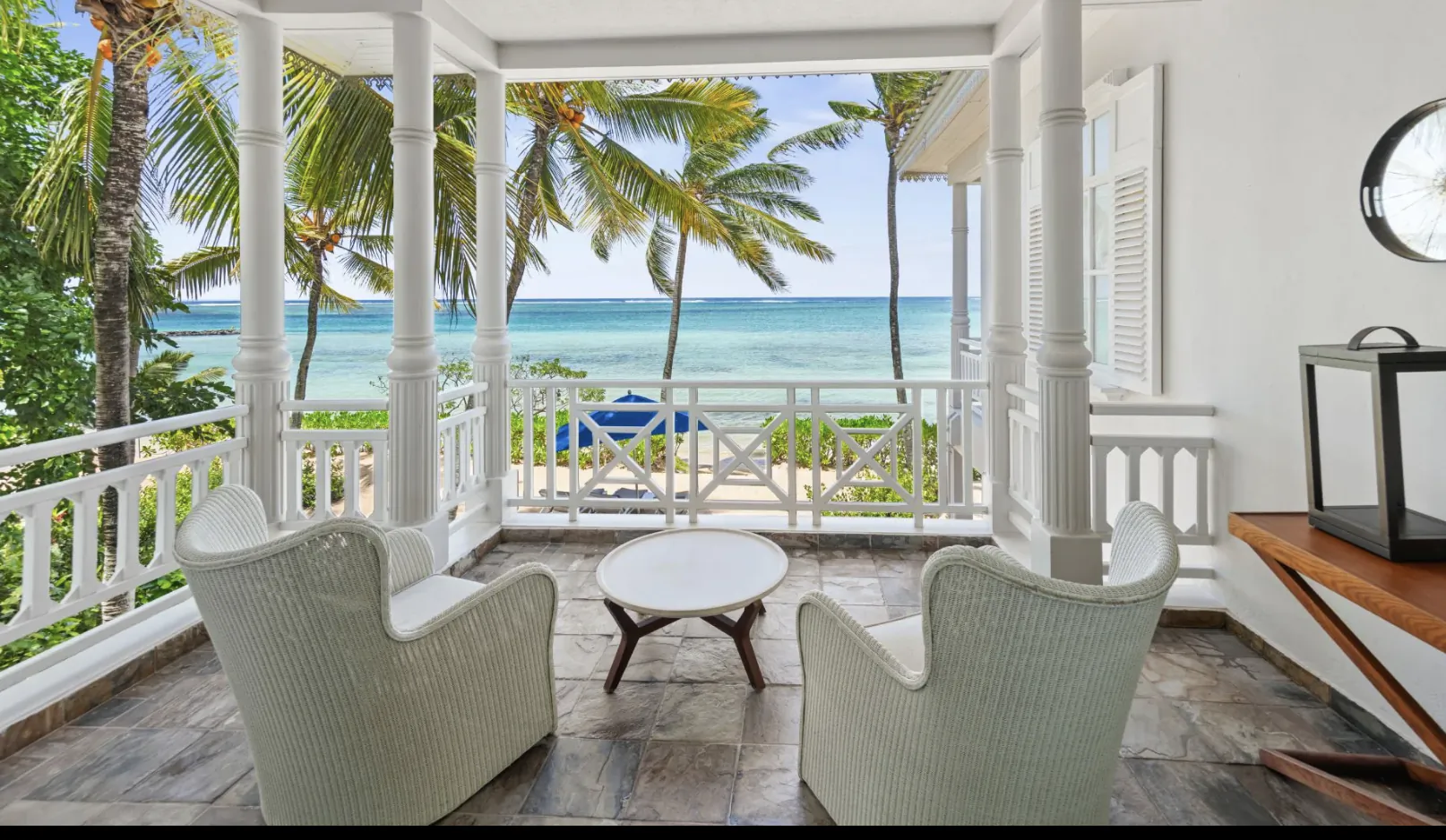Oceanfront veranda with two white wicker chairs, round table, and palm trees overlooking turquoise sea at Heritage Le Telfair Mauritius