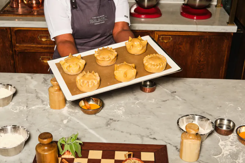 Chef holding a tray of six golden pies in a professional kitchen at Rosewood London