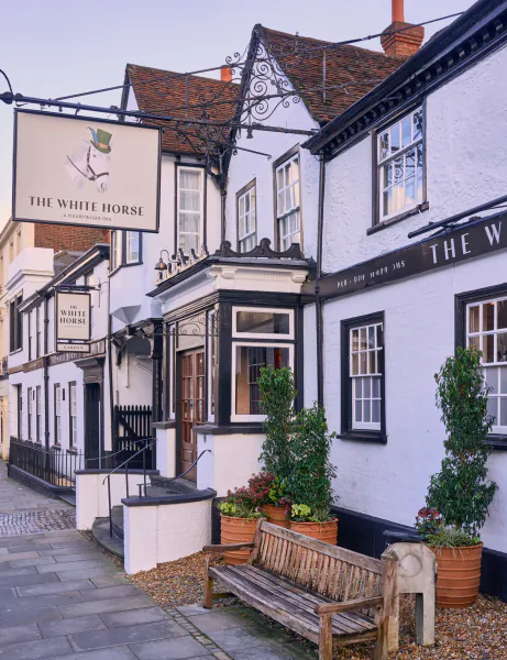 The White Horse pub in Dorking, UK, with hanging sign, white facade, wooden bench and potted plants outside