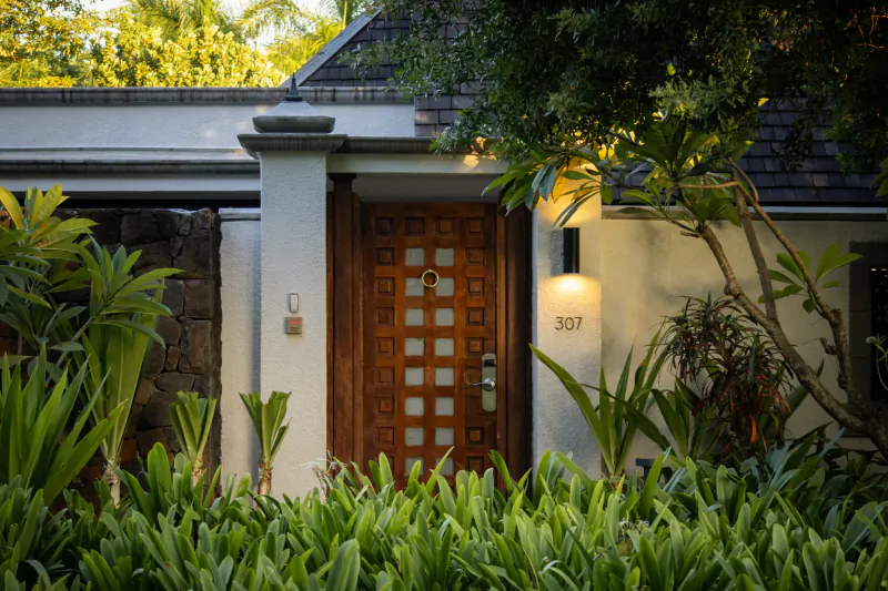 Wooden front door of villa 307 with warm lighting, surrounded by lush tropical plants and greenery