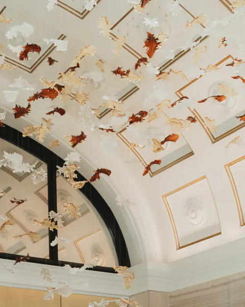 Hundreds of white and amber glass fish mobiles suspended from an ornate white ceiling with gold trim