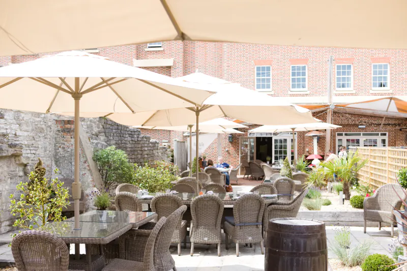 Outdoor patio at Hotel Du Vin with wicker tables, chairs and large beige umbrellas against a brick building