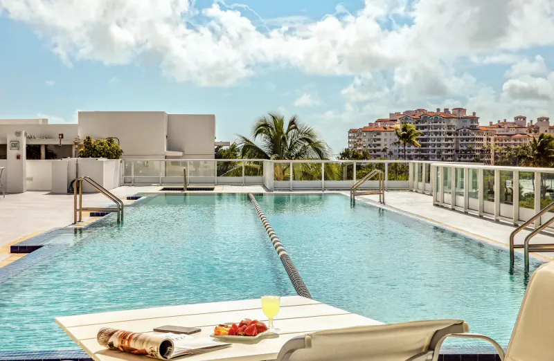 Rooftop infinity pool with lounge chair, fruit plate and drink overlooking city buildings and palm trees