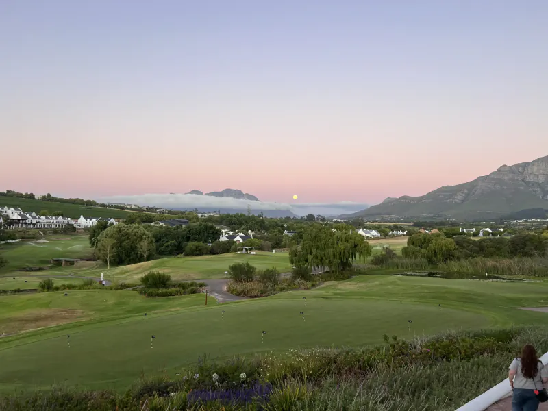 Golf course at sunset with moon rising over misty mountains and resort buildings
