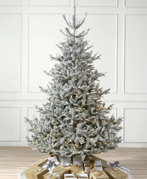Flocked white Christmas tree with warm white lights and wrapped gold gift boxes at its base