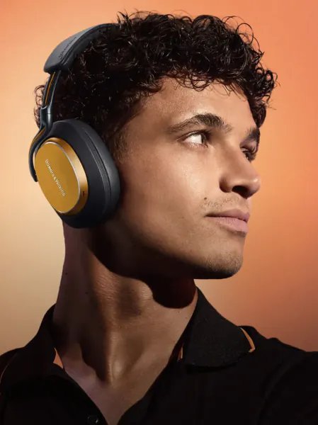Man wearing black and gold Bowers & Wilkins headphones, looking right against an orange background