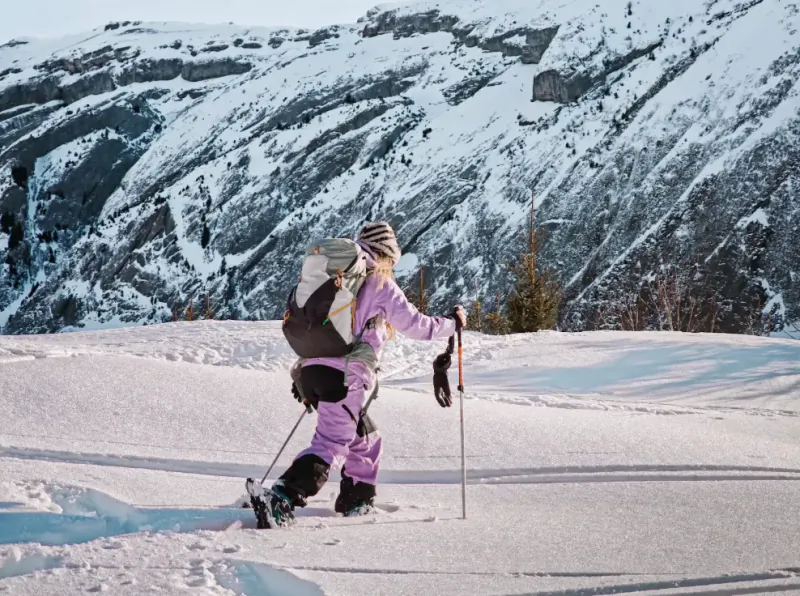 Woman in purple snowsuit skiing uphill with poles on snowy mountain slope