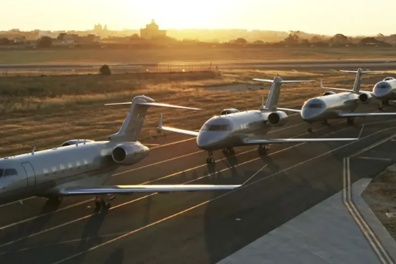 Four silver private jets parked in a row on an airport tarmac at sunset