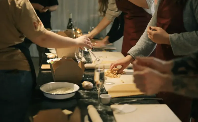 Group of people making fresh pasta together at a cooking class, hands rolling dough and handling ingredients on a kitchen counter
