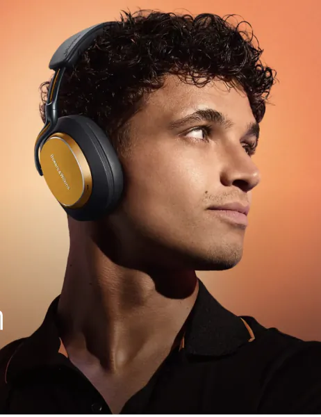 Man wearing black and gold Bowers & Wilkins headphones, looking right against an orange background