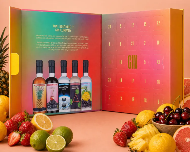 Open That Boutique-y Gin Company advent calendar with 24 numbered doors, four gin bottles, and fresh fruits on a pink surface