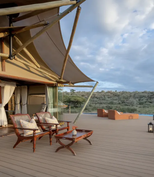 Luxury safari tent deck with two wooden lounge chairs, coffee table, and panoramic savanna view