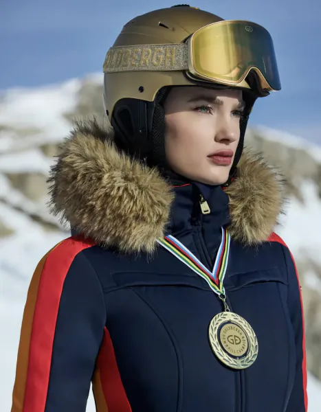 Woman in gold ski helmet and navy jacket with fur hood wearing a gold medal on snowy mountain slope
