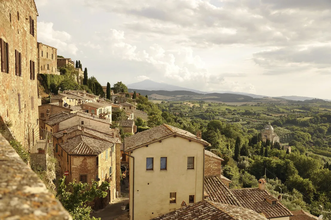 Tuscan hillside village with terracotta roofs overlooking rolling green hills and distant mountains