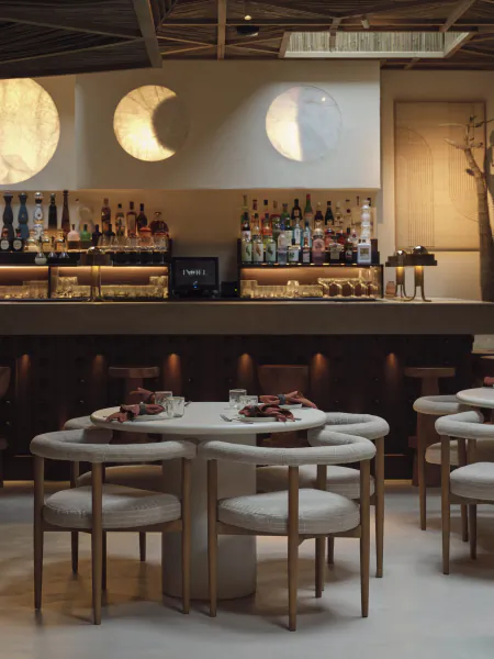 Modern bar interior with round table, curved chairs, backlit bottles, and three circular wall lights