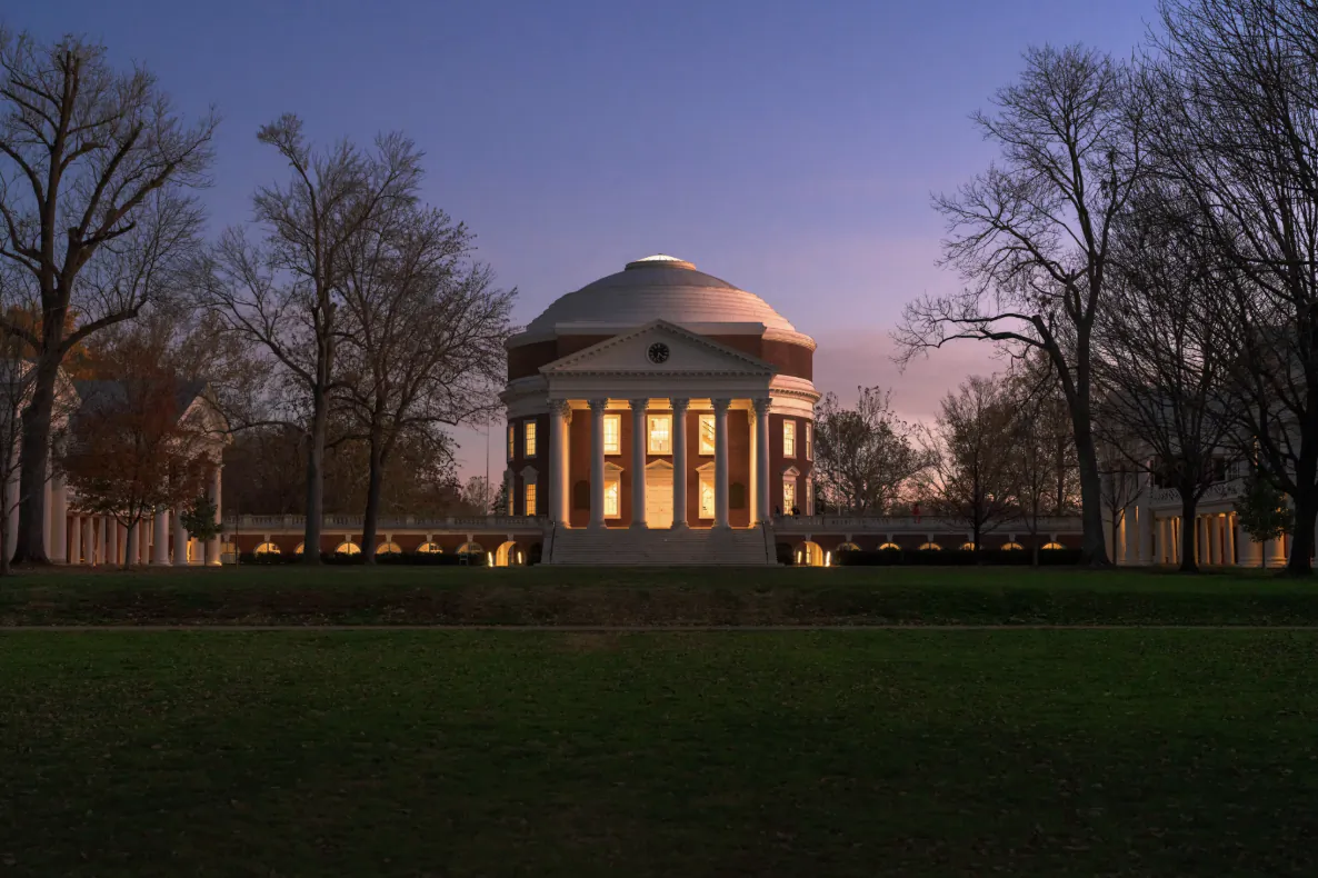 Illuminated neoclassical rotunda with glowing columns at dusk, surrounded by bare trees and manicured lawn