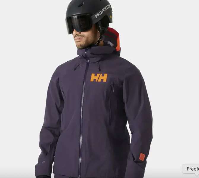 Man wearing a dark purple Helly Hansen ski jacket with orange HH logo, black Marker helmet and goggles
