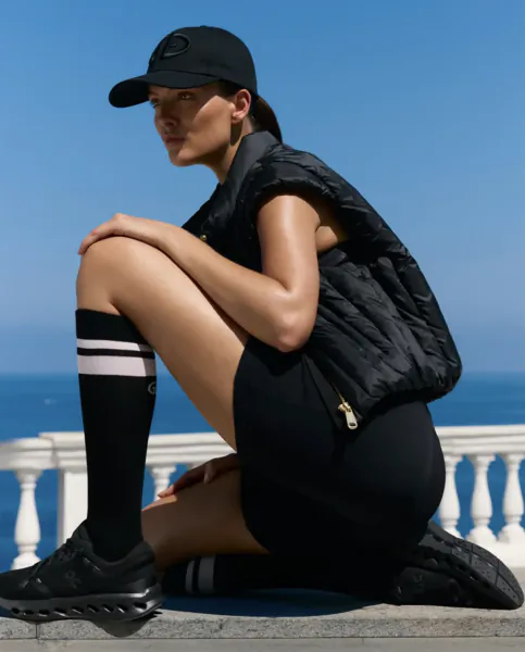 Woman in black athletic wear and cap crouching outdoors by the ocean