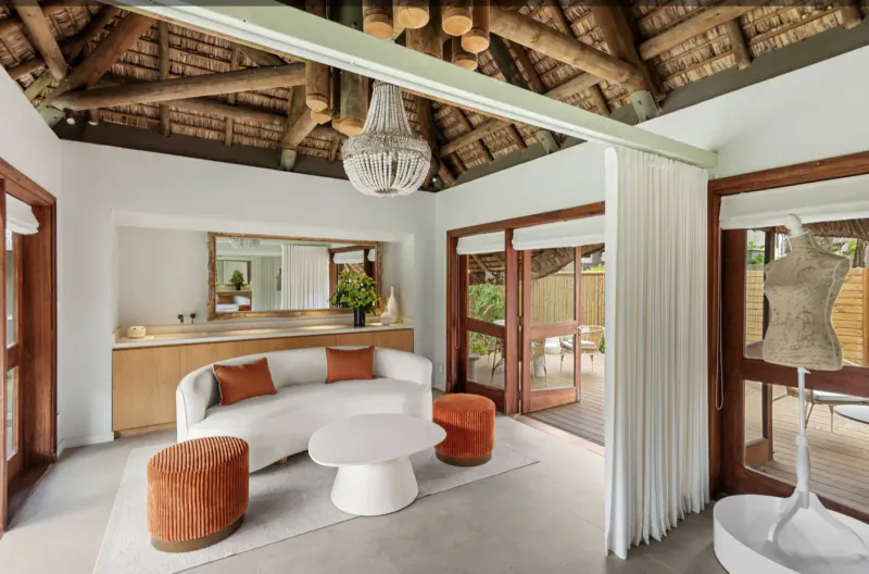 Modern living room with curved white sofa, orange ottomans, white coffee table, and thatched ceiling with chandelier