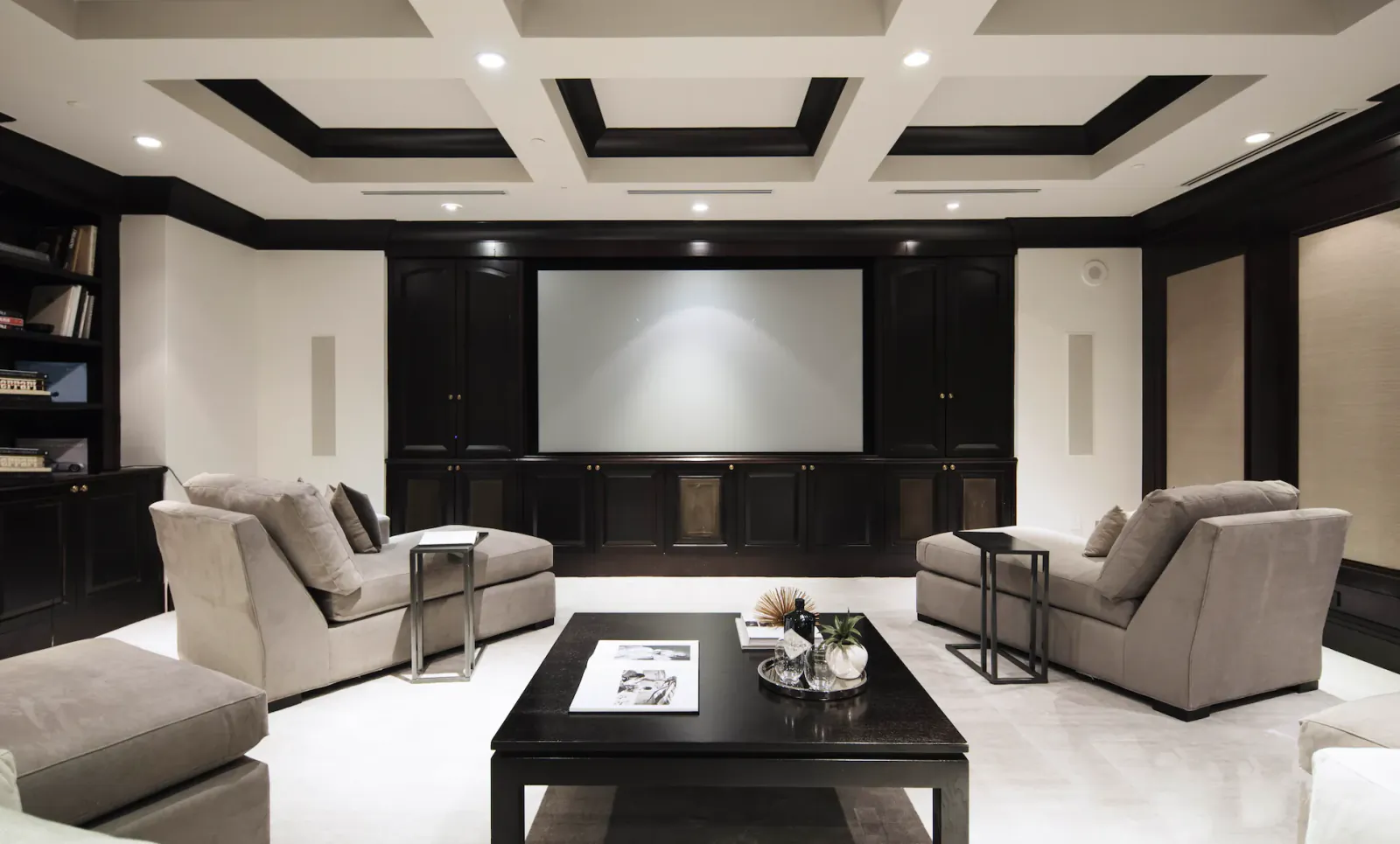 Modern home theater with two beige sofas, black coffee table, and large projector screen in a dark wood-paneled room