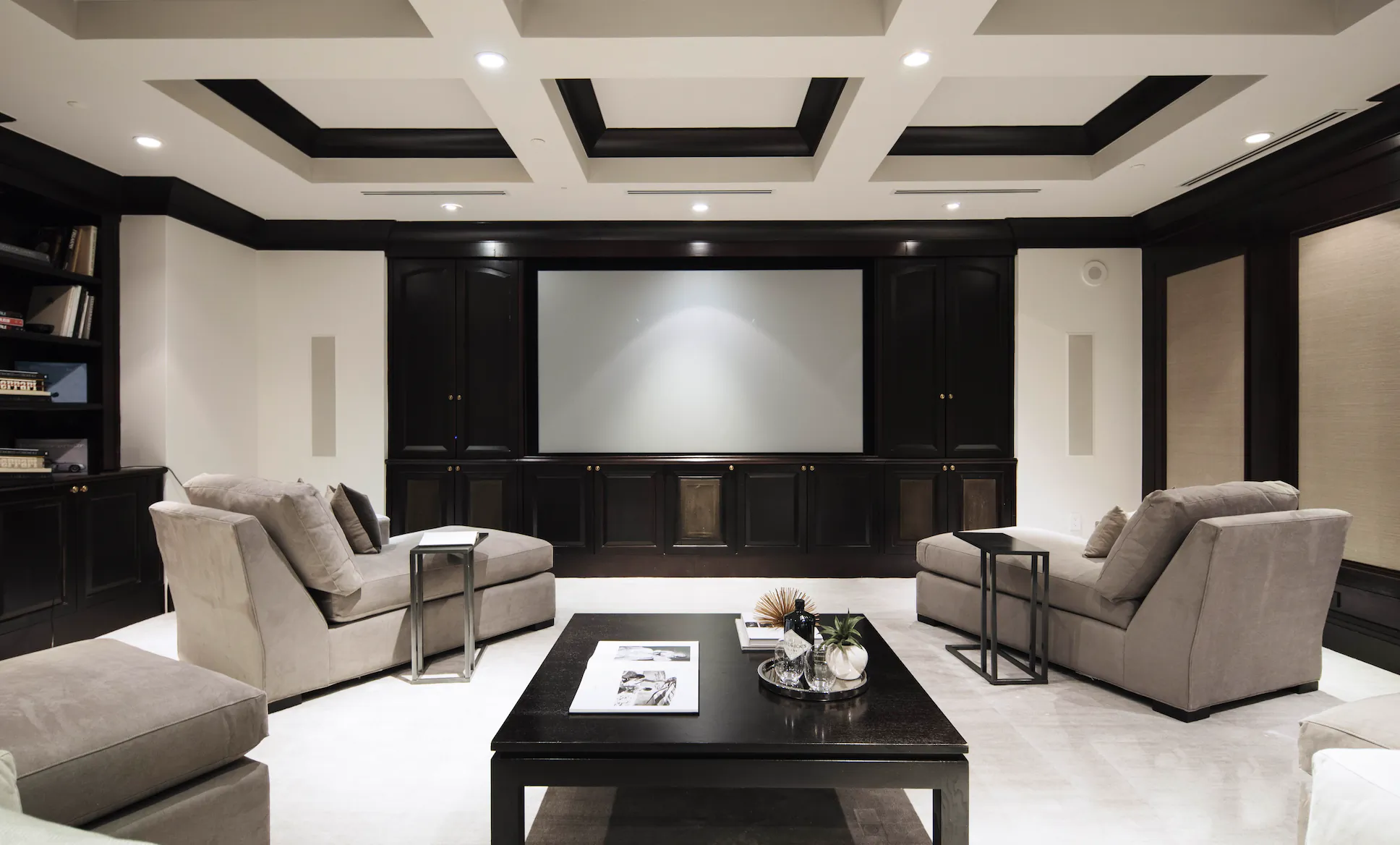 Modern home theater with two beige sofas, black coffee table, and large projector screen in a dark wood-paneled room