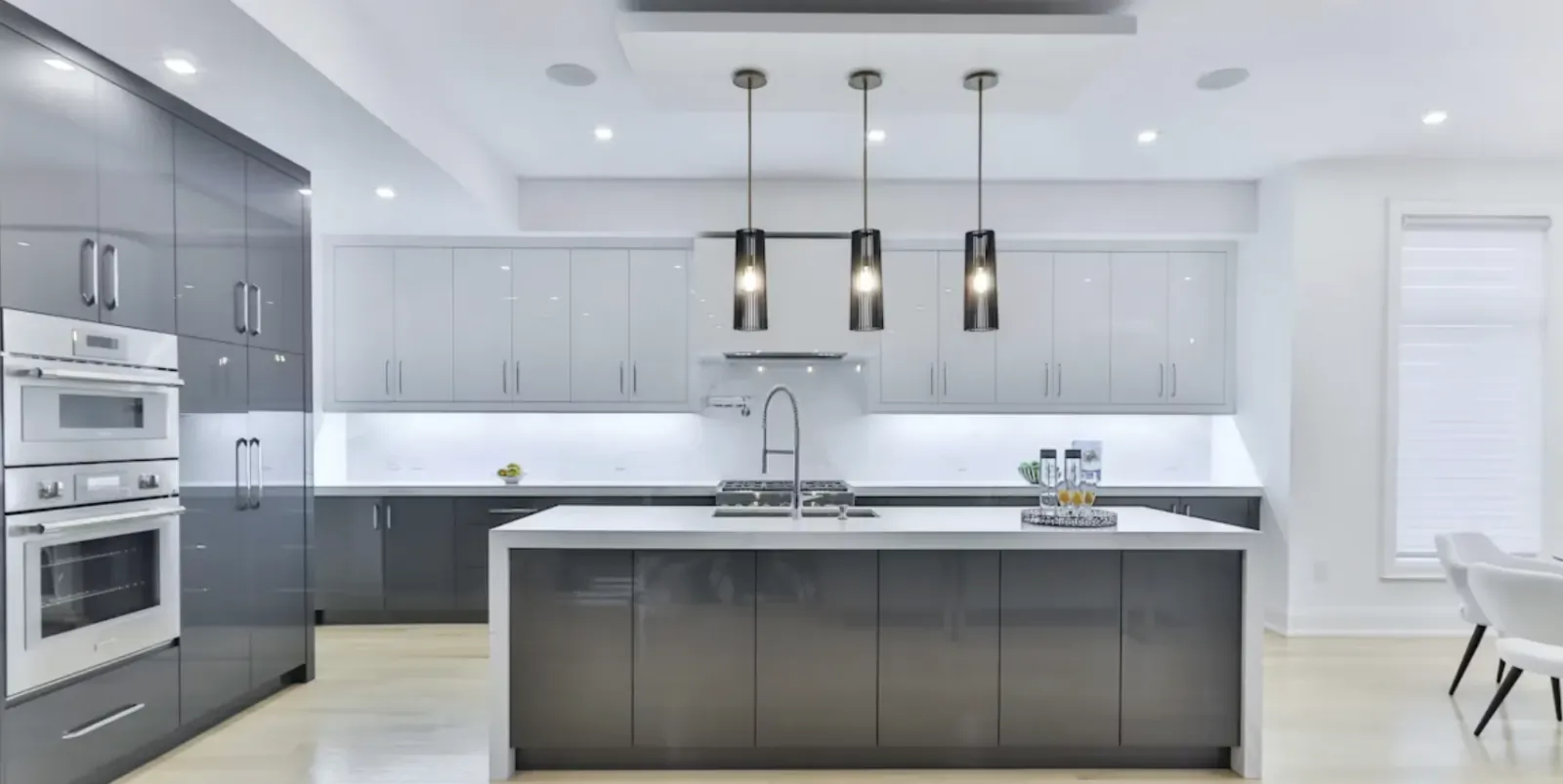 Modern kitchen with grey cabinets, white island, stainless steel appliances, and three pendant lights