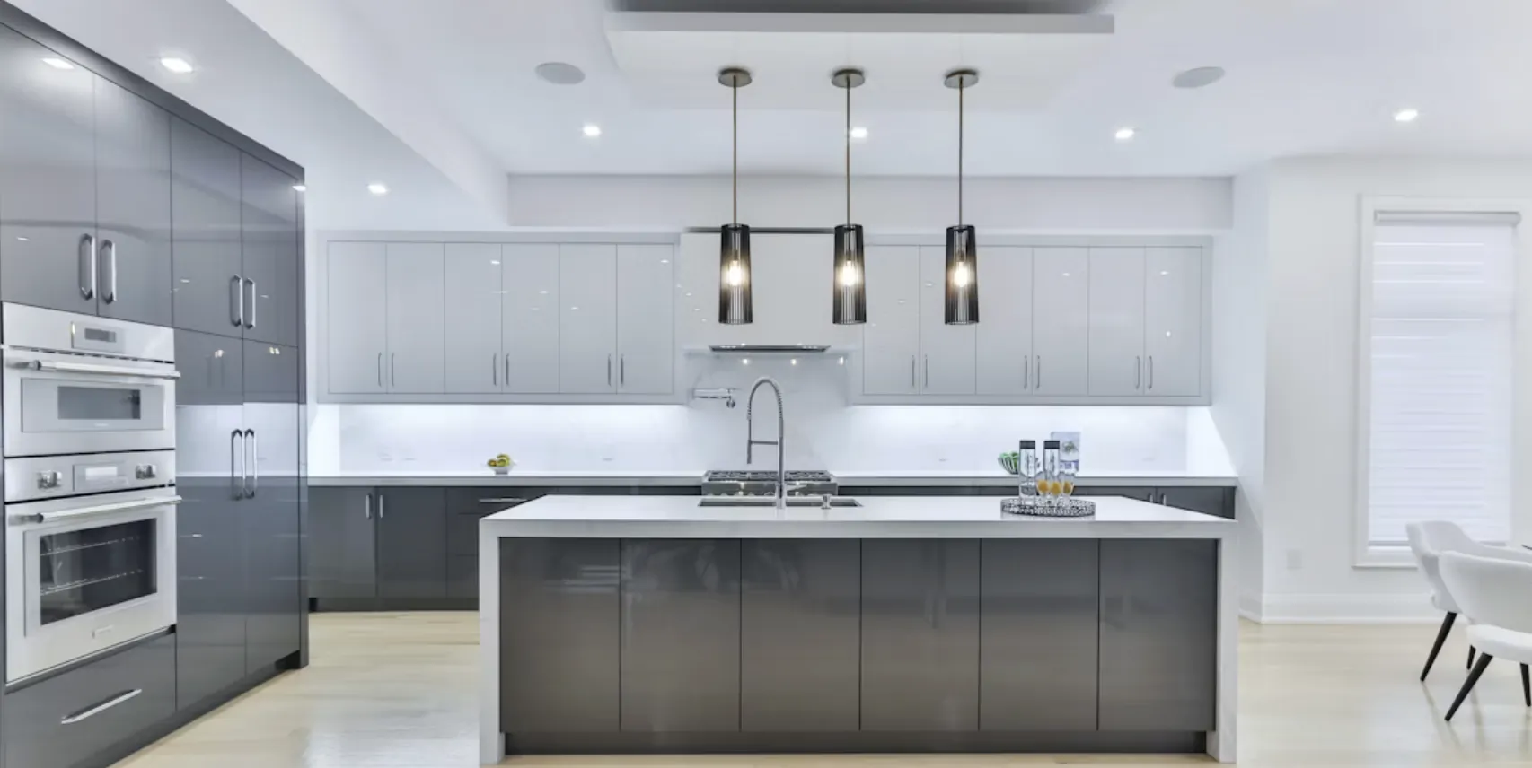 Modern kitchen with grey cabinets, white island, stainless steel appliances, and three pendant lights
