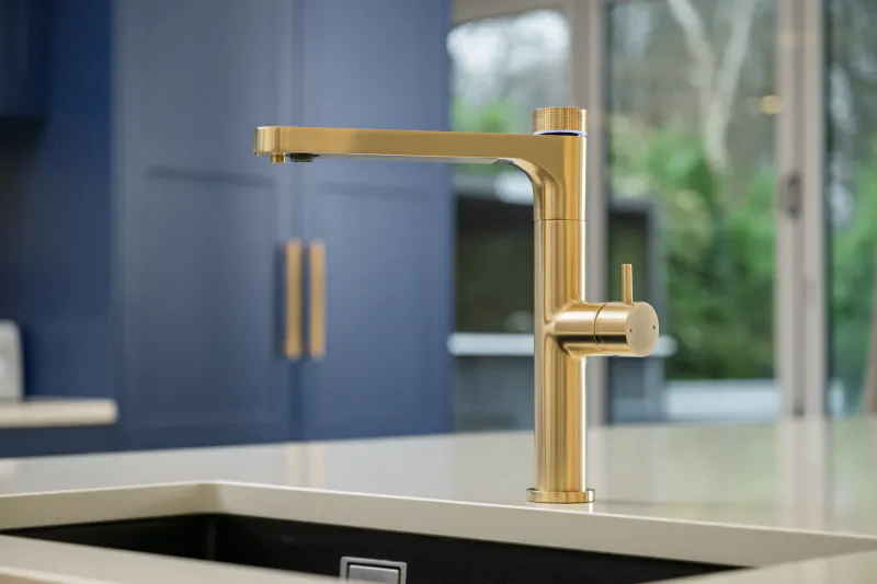 Modern brushed gold kitchen faucet with lever handle on white countertop against blue cabinets