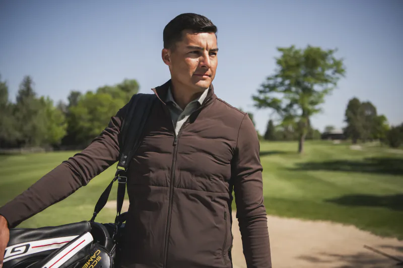 Man in brown vest carrying golf bag on sunny course