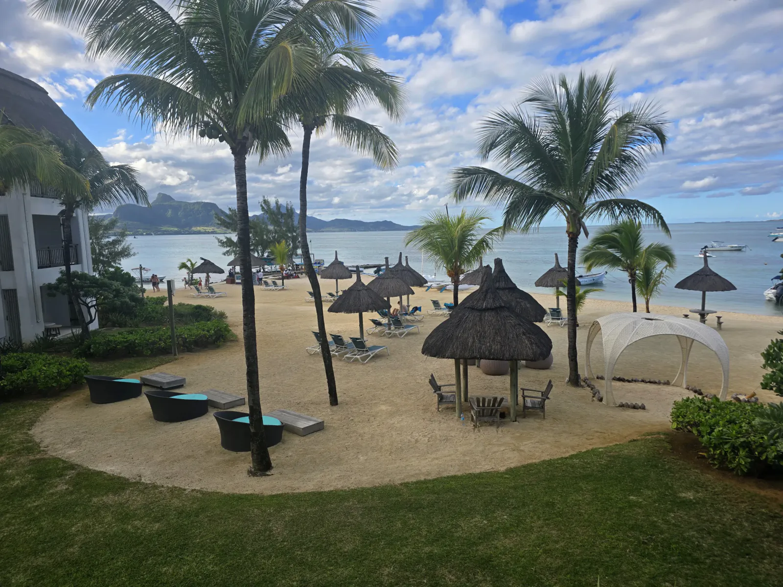 Tropical beach resort with palm trees, thatched umbrellas, lounge chairs, and ocean view under blue sky