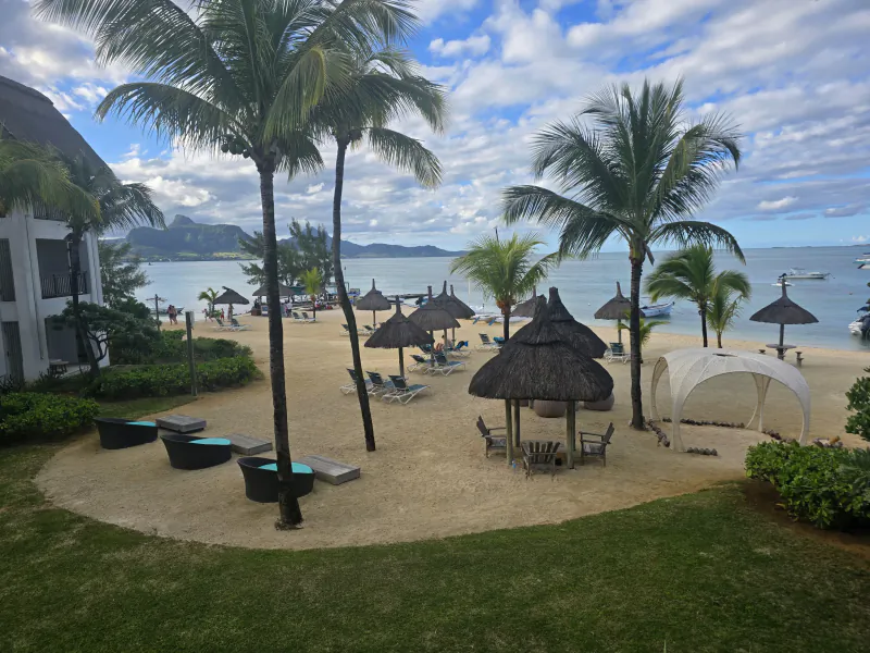 Tropical beach resort with palm trees, thatched umbrellas, lounge chairs, and ocean view under blue sky