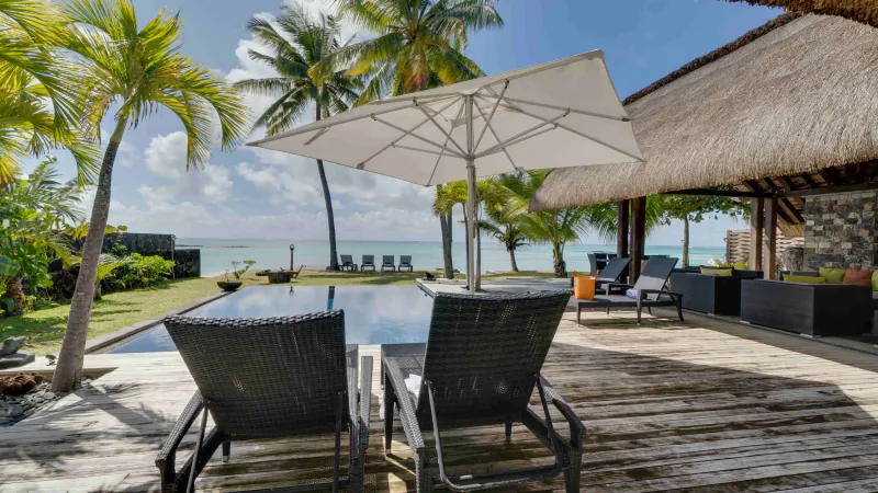 Luxury villa deck with two wicker lounge chairs, white umbrella, and ocean view in Mauritius