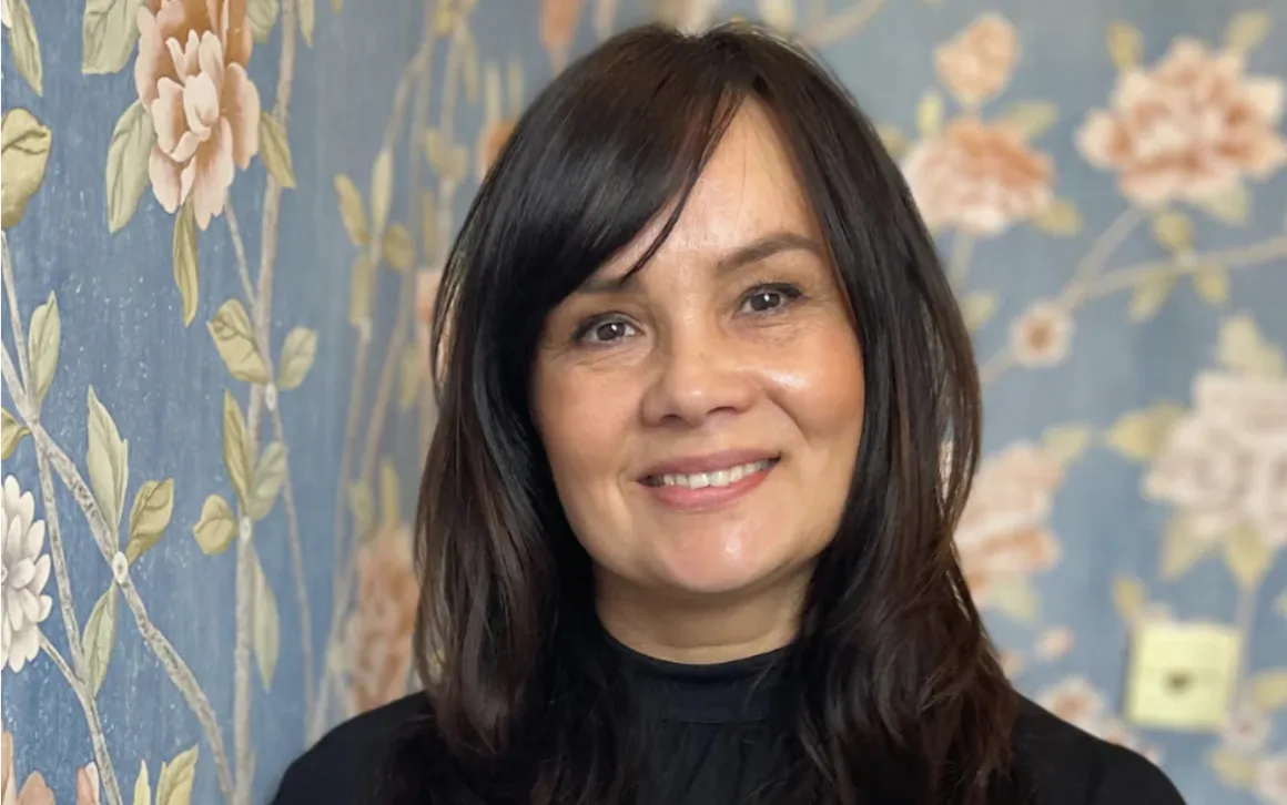 Smiling woman with long dark hair in front of blue floral wallpaper