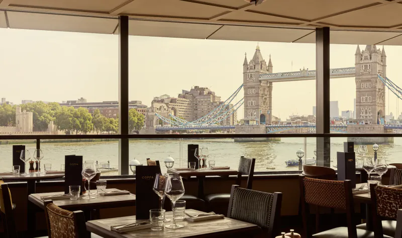 Elegant restaurant interior with Tower Bridge view through large windows, set tables with wine glasses and menus