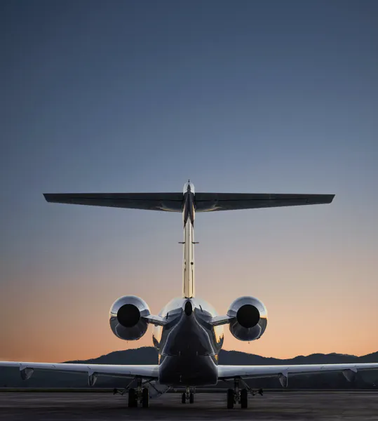 Rear view of a private jet on a runway at sunset with mountains in the background