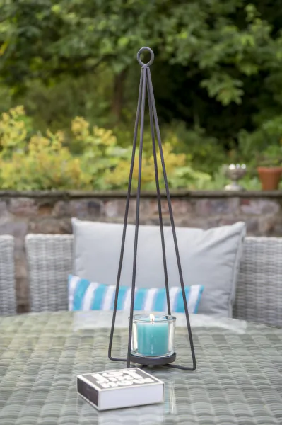 Tall black metal candle holder with lit teal candle on outdoor patio table, matchbox beside it