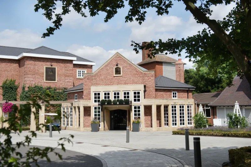 The Belfry hotel entrance: red brick building with arched windows, covered porch, and landscaped courtyard under a blue sky