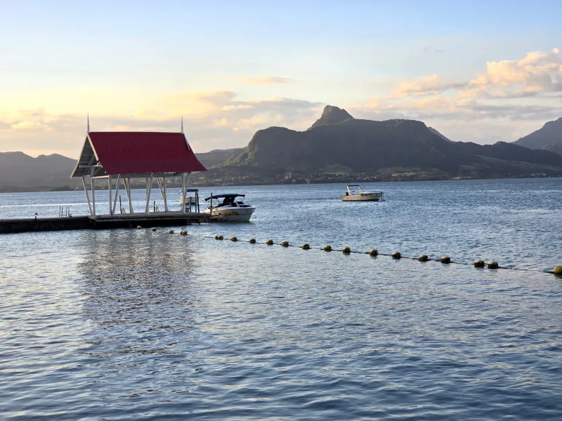 Red-roofed pier with docked boats on calm water, mountains in the background at sunset