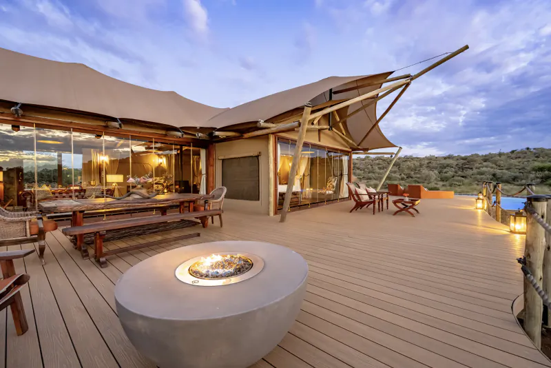 Luxury safari lodge deck at dusk with fire pit, lounge seating, and panoramic savanna view
