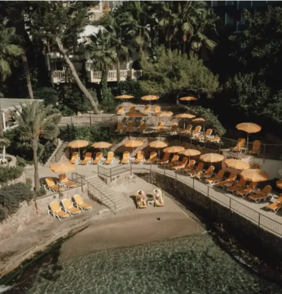 Aerial view of a resort pool deck with rows of orange lounge chairs and matching umbrellas overlooking the water