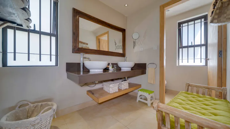 Modern bathroom with double vessel sinks, wooden vanity, large mirror, and green bed in foreground