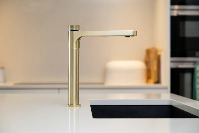 Brushed gold kitchen faucet with blue LED light on white countertop