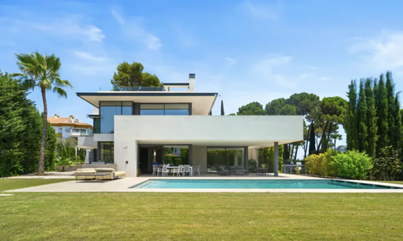 Modern luxury villa with pool, lawn, and palm trees under blue sky in Marbella