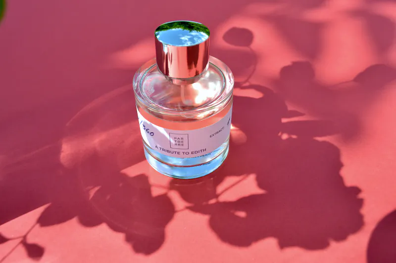 Parterre Fragrances perfume bottle on pink surface with leaf shadows, labeled 'A Tribute to Edith'